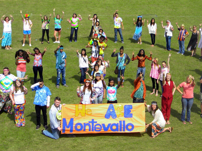 A group of young people dressed in hippie costumes and holding a banner that reads "We are Montevallo"